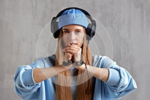 A young charming red-haired woman in a blue sweater and cap with DJ headphones on her head folded her hands in a prayer
