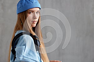 Young charming red-haired woman in a blue sweater and cap with DJ headphones on her shoulder looks at the camera. Music