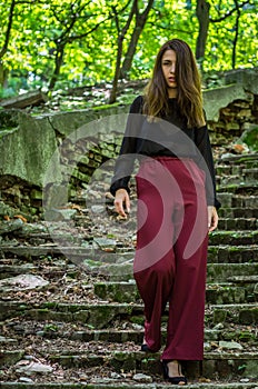 Young charming teenager girl with long dark hair is a graceful gait destroyed by an ancient staircase the steps in Striysky Park