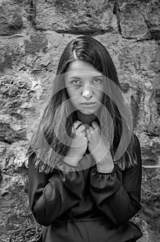 Young charming teenager girl with long dark hair standing near the ruins of the ancient castle fortress with a sad expression on