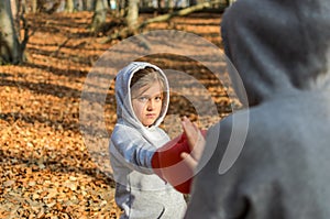 Young charming woman boxing trainer in a tracksuit with a hood on her head, trains a little child girl in red boxing mittens at bo
