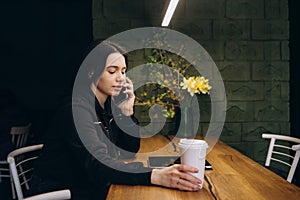 Young charming woman calling with cell telephone while sitting alone in coffee shop during free time