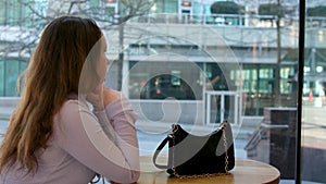 Young charming woman calling with cell telephone while sitting alone in coffee shop during free time, attractive female