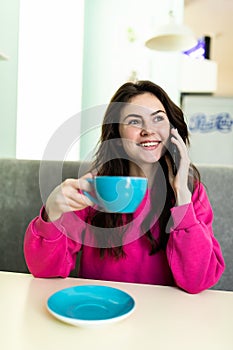 Young charming woman calling with cell telephone while sitting alone in coffee shop during free time. Attractive female with cute