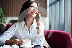 Young charming woman calling with smartphone while sitting alone in coffee shop during free time, attractive female with