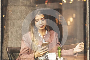 Young charming woman with cell telephone while sitting alone in coffee shop during free time, attractive female having looking