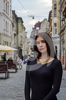 Young charming woman with long curly hair, strolling among the old town of Lviv architecture in black dress