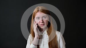 Young charming woman with long ginger hair talking on cell phone, girl in white shirt isolated on black background