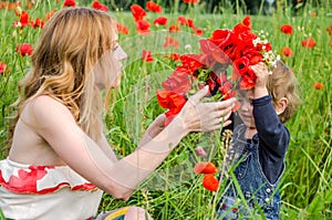 Young charming woman with long hair mom with her daughter walking on the field among the grass, wove a wreath, a bouquet of red po