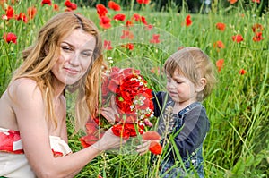 Young charming woman with long hair mom with her daughter walking on the field among the grass, wove a wreath, a bouquet of red po