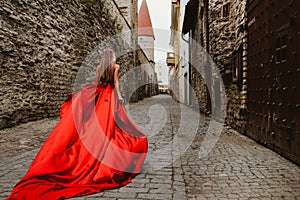 Young gorgeous woman in long red dress walking in Medieval town