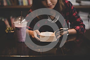 Young charming woman with milkshake and reading book sitting ind