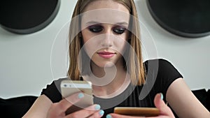 Young charming women with heavy make up rewriting text on phone from card, black and white wall background