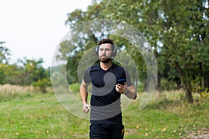 Young cheerful active guy sporty walking with headphones mobile phone enjoying listening to music, jogging outdoors on urban city