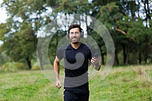 Young cheerful active guy sporty walking with headphones mobile phone enjoying listening to music, jogging outdoors on urban city