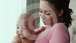 Young cheerful african american mother nursing her newborn baby, cuddling him and smiling at home, slow motion