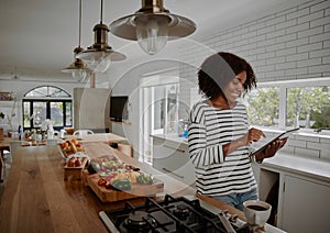 Young cheerful african american woman checking recipe on digital tablet while preparing vegetable salad in kitchen