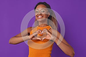 Young cheerful African American woman in glasses shows heart shape from fingers