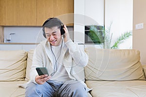 asian guy listening to music in headphones sitting on sofa at home. A man alone on the couch feels good lifestyle.