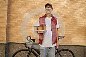 Young cheerful asian male courier holding four cups of coffee an
