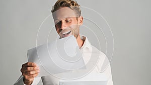 Young cheerful bearded businessman in shirt opening envelope with business documents and rejoicing on camera isolated on