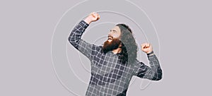 Young cheerful bearded man with long hair celebrating victory over grey background