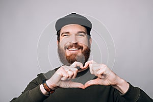 Young cheerful bearded man showing heart gsture with both hands.