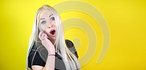 Young cheerful blonde girl is calling and talking on the phone, posing on a yellow studio background.