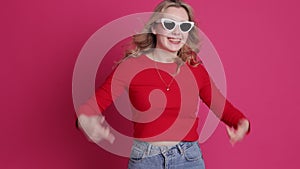 Young cheerful blonde woman with big smile having fun, shows teeth with braces, gestures with thumb up, dances on pink