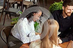 Young cheerful business people, colleagues sitting together in cafe, meeting after work and spending good time together