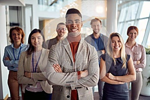 A young cheerful businessman is standing in the company building hallway with his colleagues and enjoys posing for a photo.