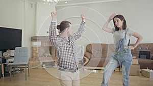 Young cheerful Caucasian couple dancing in the living room with unpacked furniture. Happy family moving in new house