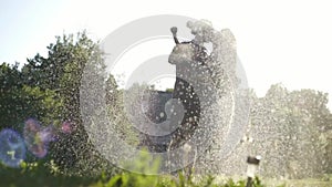 Young cheerful couple hosing the garden and playing under sprays of water