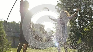 Young cheerful couple hosing the garden and playing under sprays of water