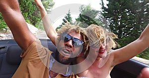 Young cheerful couple singing while driving in convertible