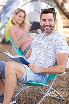 young and cheerful couple sitting reading near tent