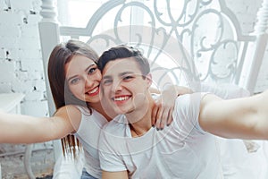 Young cheerful couple taking selfie pictures with a smart phone in bedroom. Celebrating Saint Valentine`s day together