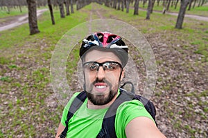 Young cheerful cyclist taking photo of himself in forest alley