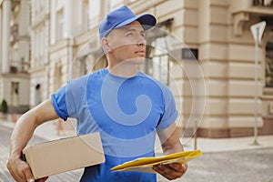 Young cheerful delivery man with parcel cardboard box on the city streets