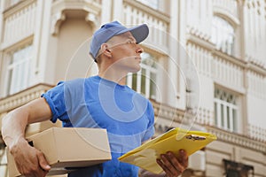 Young cheerful delivery man with parcel cardboard box on the city streets