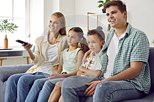 Young cheerful family with children relax watching television programs together.