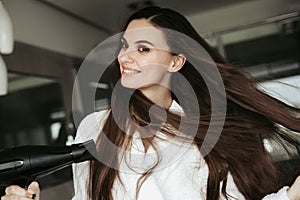 Young cheerful female drying hair with blowdryer