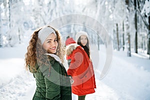 Young cheerful friends on a walk outdoors in snow in winter forest, looking back.