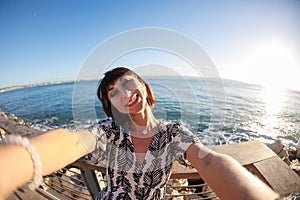 A young and cheerful girl in a dress takes a selfie on the beach