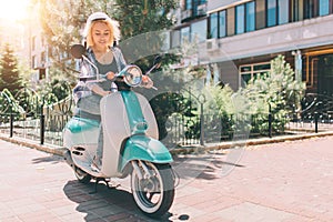 Young cheerful girl driving scooter in in city. Portrait of a young and stylish woman with a moped