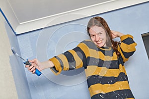 Young cheerful girl painting wall with paint roller.