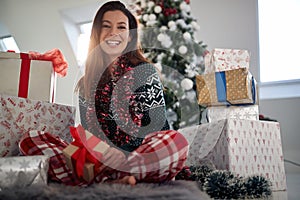 A young cheerful girl sitting on the floor and posing for a photo surrounded by Xmas presents. Christmas, relationship, love,