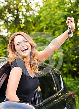 Young cheerful joyful smiling gorgeous woman holding up keys to her first new car. Customer satisfaction