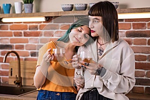 Young cheerful lesbian caucasian couple drinking tea or coffee and enjoying time together at home kitchen. Concept of