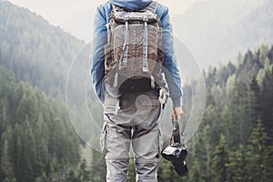 Young cheerful man photographer holding digital camera in a mountains. Photography, travel and active lifestyle c